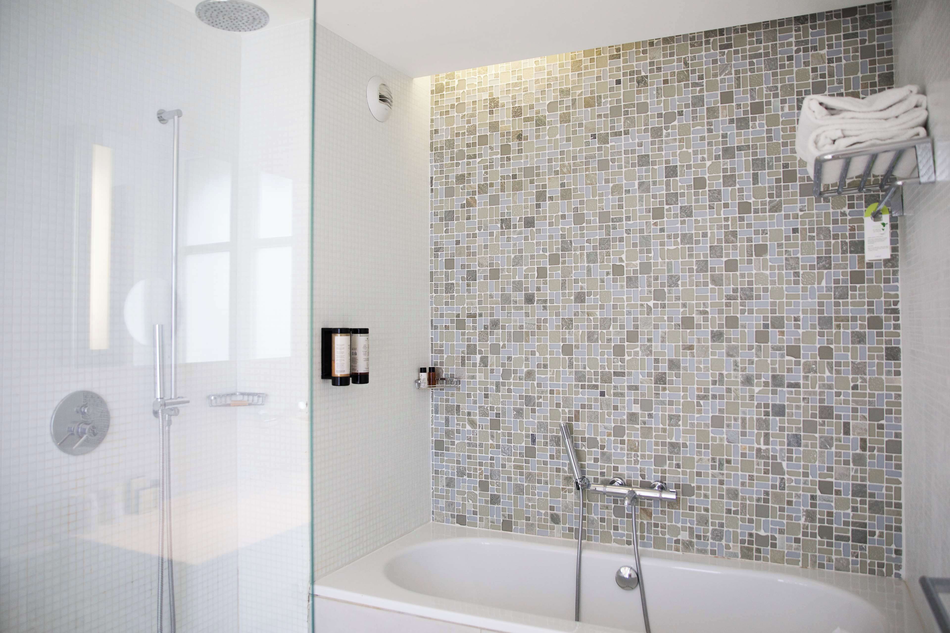 A modern bathroom with a glass-enclosed shower, a freestanding bathtub, and a mosaic tile wall.