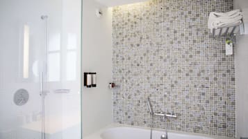 Un baño moderno con ducha envuelta en vidrio, una bañera independiente y un muro de mosaicos.