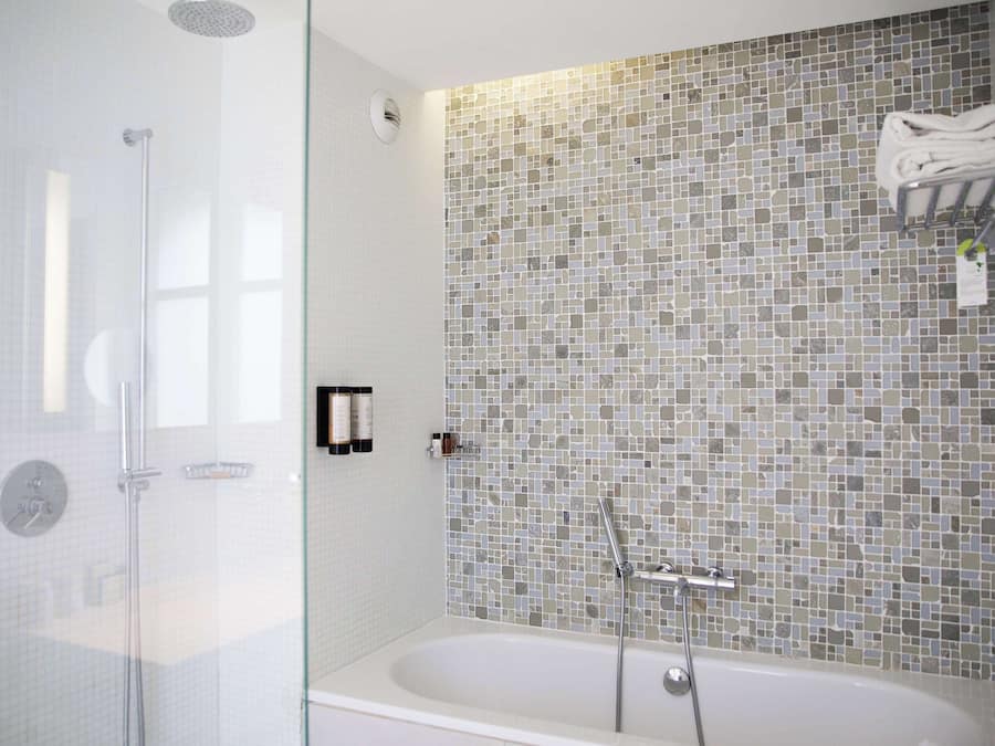 Un baño moderno con ducha envuelta en vidrio, una bañera independiente y un muro de mosaicos.