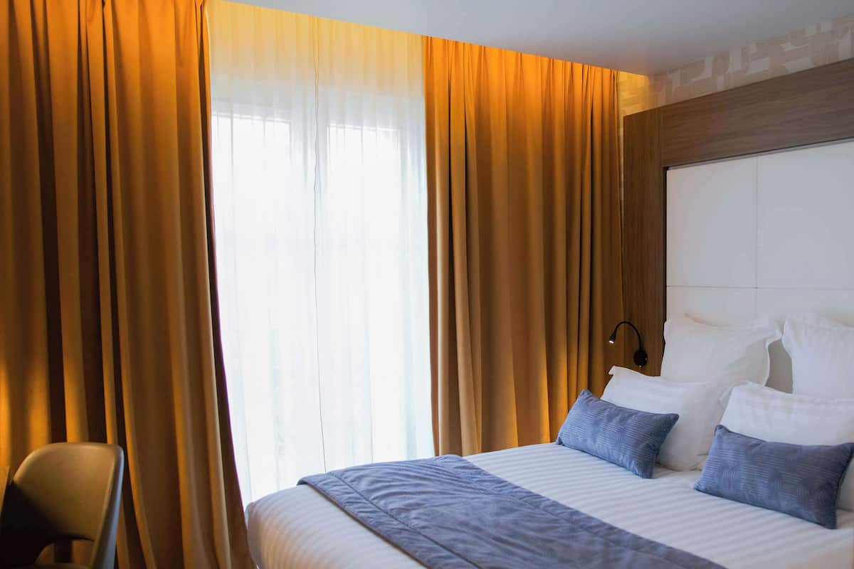 A hotel room with a large bed, two pillows, a chair, and curtains.