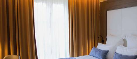 Habitación de hotel con una cama grande, dos almohadas, una silla y cortinas.