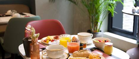 A breakfast table with various food items, a glass of orange juice, and a vase with flowers.