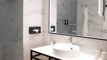 Un baño moderno con pared de azulejos de mármol, un lavamanos blanco y redondo, un espejo grande y un perchero para toallas.