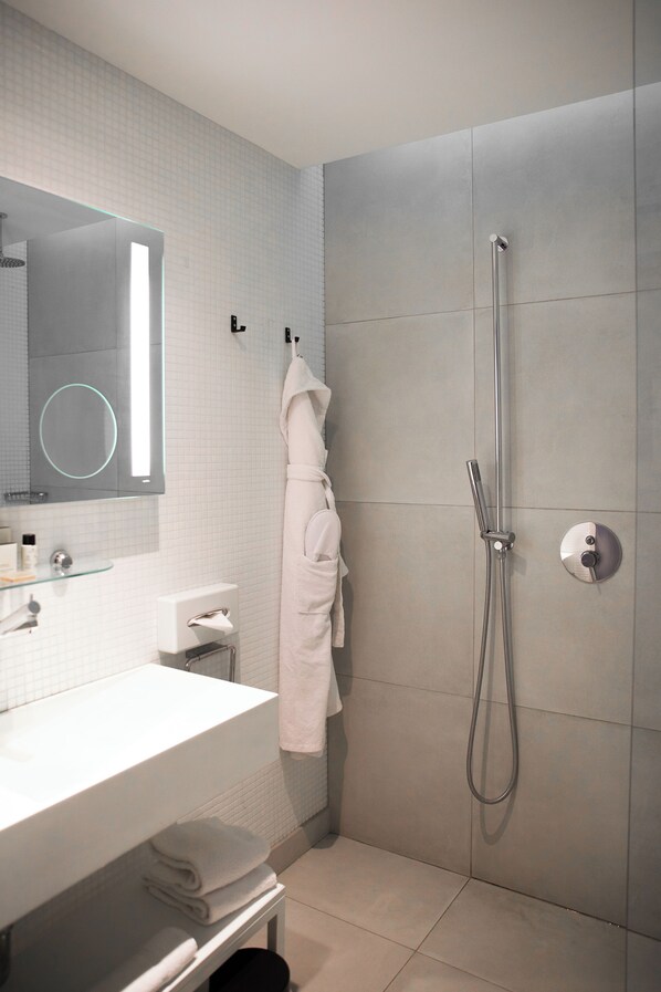 A modern bathroom with a white sink, a glass mirror, a towel rack, and a shower with a handheld showerhead.