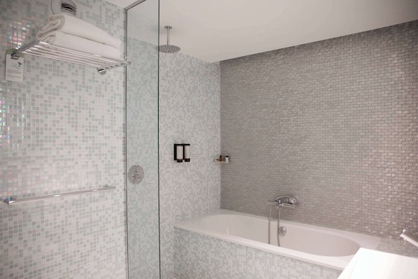 Un baño con ducha de vidrio, una bañera blanca y pared con azulejos.