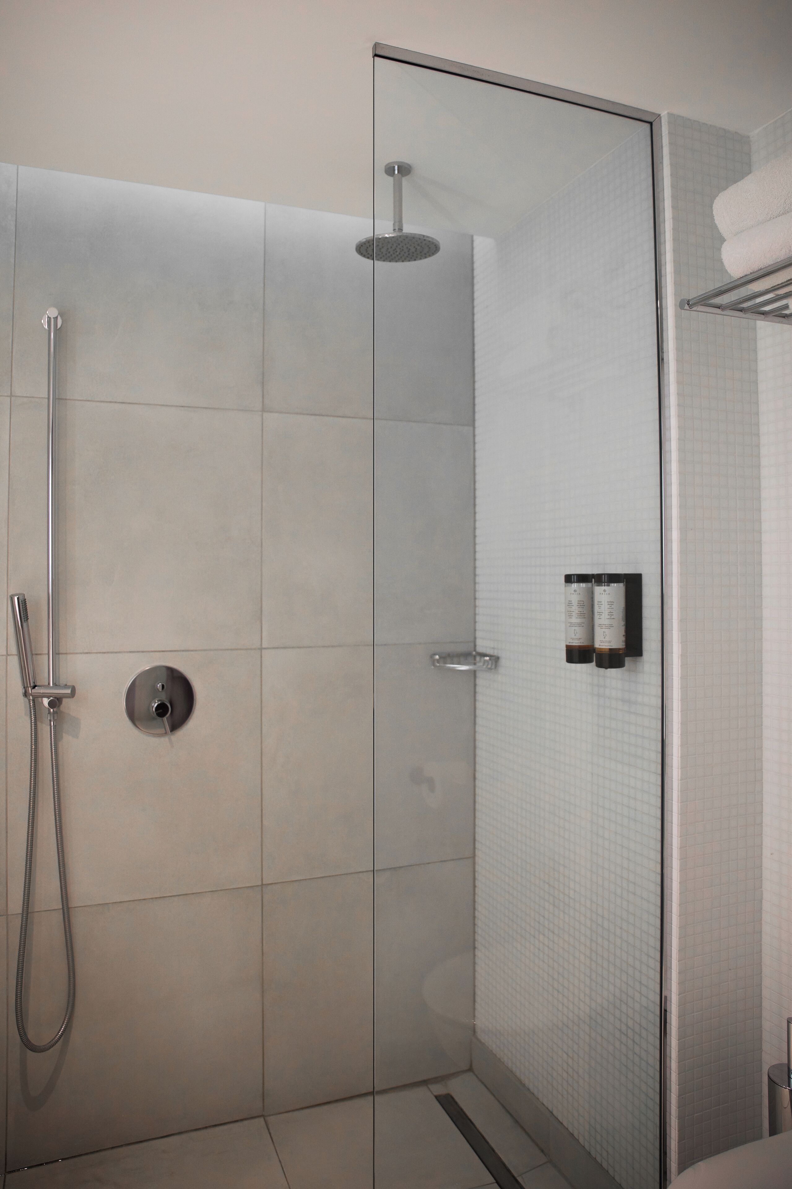 A modern shower with a glass door, a handheld showerhead, and a wall-mounted control panel.