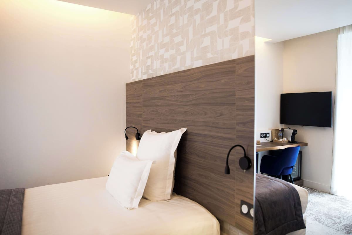A modern hotel room with a large bed, a desk with a chair, a flat-screen TV, and a wall-mounted sound system.