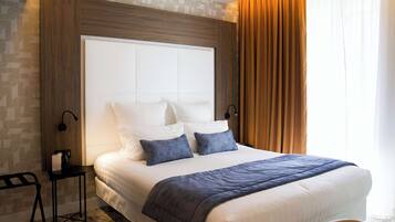 A neatly made bed with a white headboard, two pillows, and a blue throw blanket. There is a small table with a lamp beside the bed.