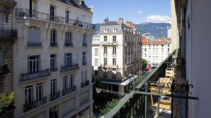 Un edificio de varios pisos con balcones, y se ve otro edificio al fondo, junto a una cadena montañosa.