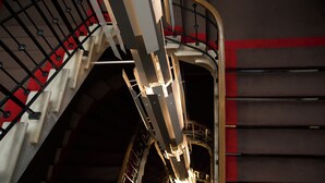 Una escalera con barandillas de metal y una franja roja en la pared.