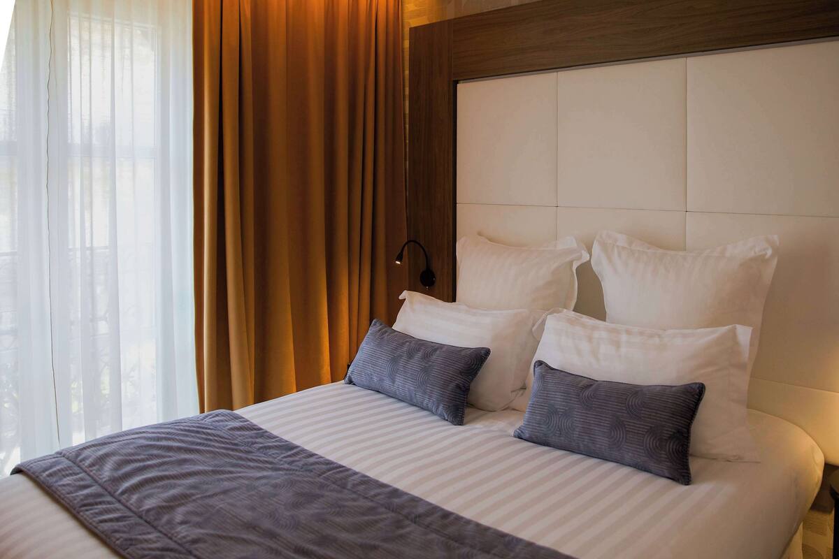 A neatly made bed with white and gray linens, a wooden headboard, and a bedside lamp.