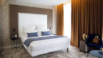 A hotel room with a large bed, a chair, a suitcase, and a small table.