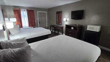 A hotel room with two beds, a desk, a TV, a microwave, and a window with curtains.