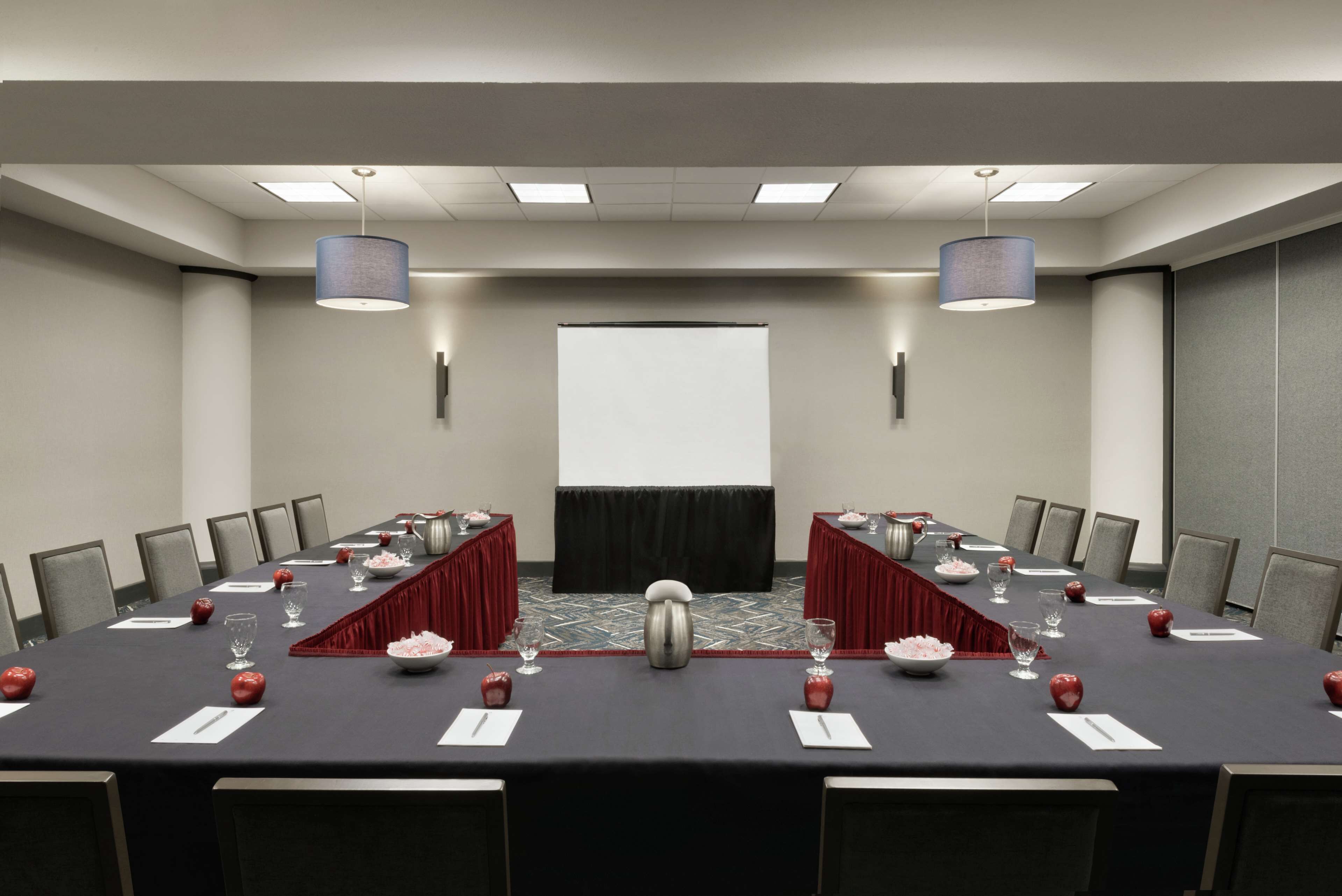 A conference room with a long table, chairs, a projector screen, and two large lamps.