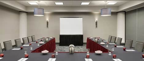 A conference room with a long table, chairs, a projector screen, and two large lamps.