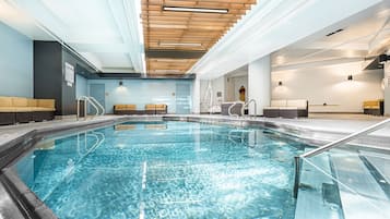 A swimming pool with clear water, wooden ceiling, and seating areas on both sides.