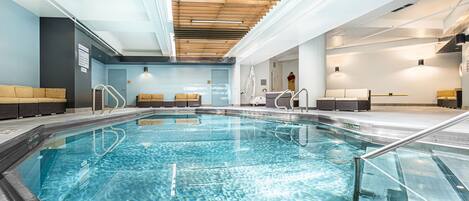 A swimming pool with clear water, wooden ceiling, and seating areas on both sides.