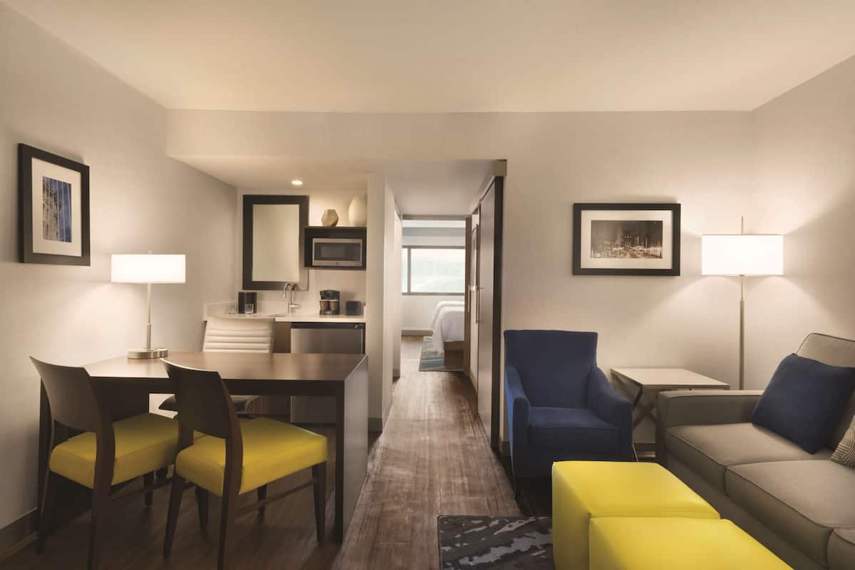 A hotel room with a dining area, a sofa, a chair, and a bed.