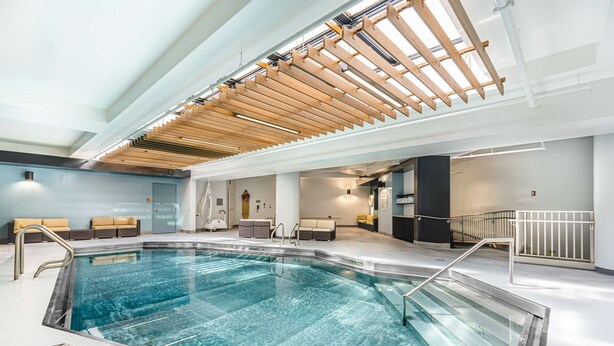 Ein modernes Hallenbad mit klarem Wasser, Holzbalkendecke und einer Sitzecke mit Sofas.