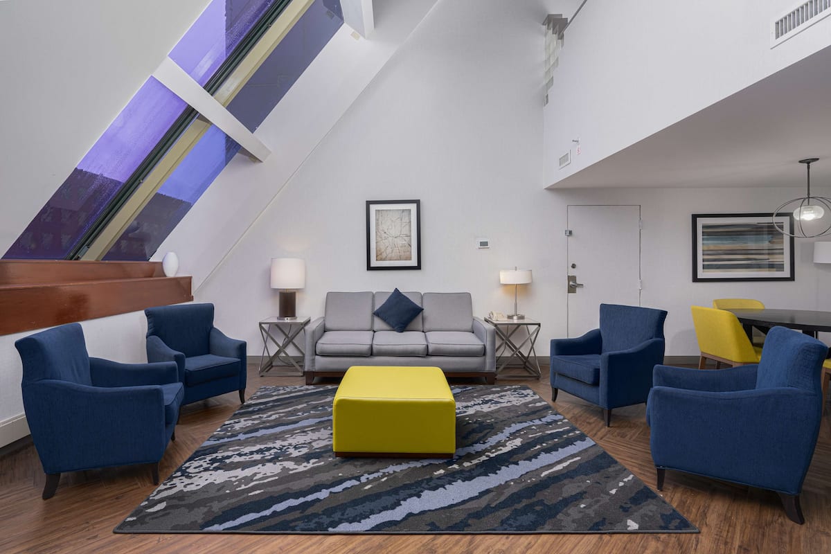 A modern living room with a sofa, armchairs, a yellow ottoman, and a patterned rug.