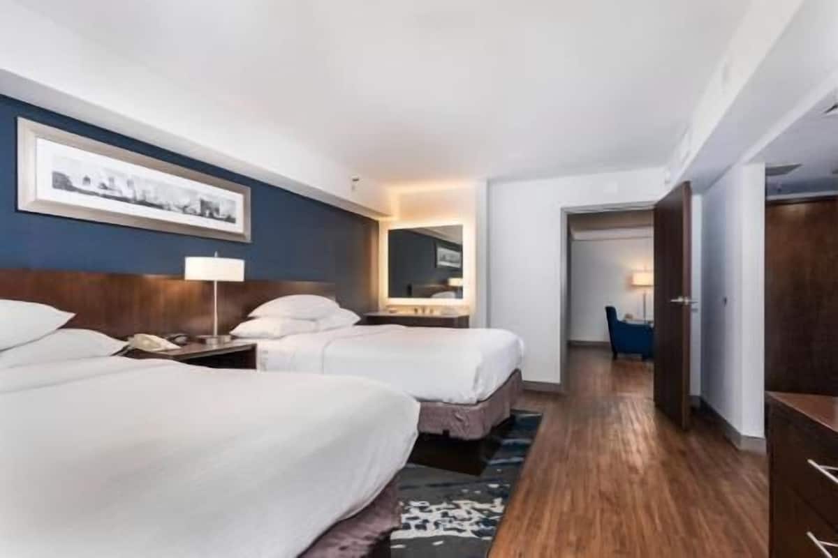 A hotel room with two beds, a desk, a chair, and a mirror.