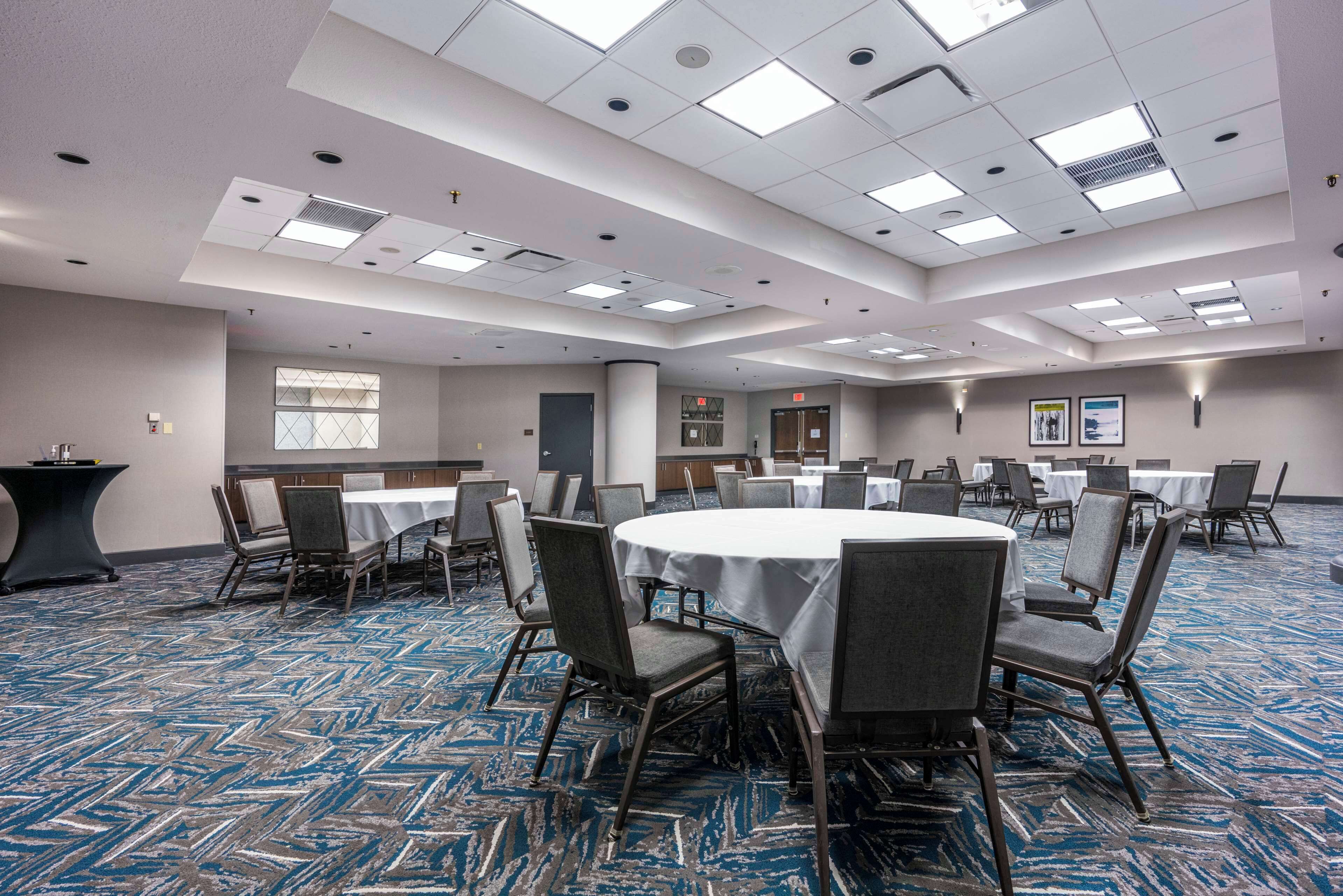 A conference room with round tables, chairs, and a carpeted floor.