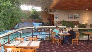 An indoor dining area with tables and chairs, a pool, and indoor plants. - Townhouse Hotel Grand Forks (Grand Forks)
