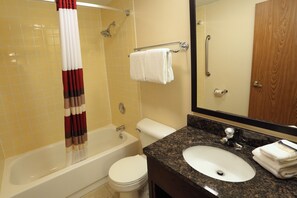 A bathroom with a bathtub, toilet, sink, and a mirror. - Townhouse Hotel Grand Forks (Grand Forks)