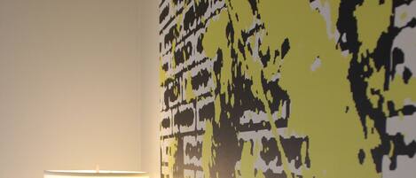 Habitación de hotel con cama, mesita de noche, lámpara y una pared con un diseño abstracto en amarillo y negro.