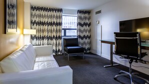 A hotel room with a white sofa, a black office chair, a desk with a television, and patterned curtains. - Comfort Inn & Suites Baltimore Inner Harbor (Baltimore)