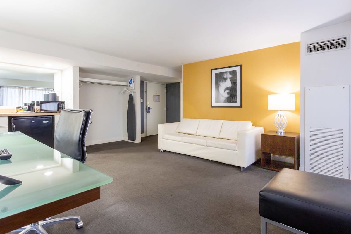 A hotel room with a glass table, a white sofa, a lamp, and a picture on the wall.