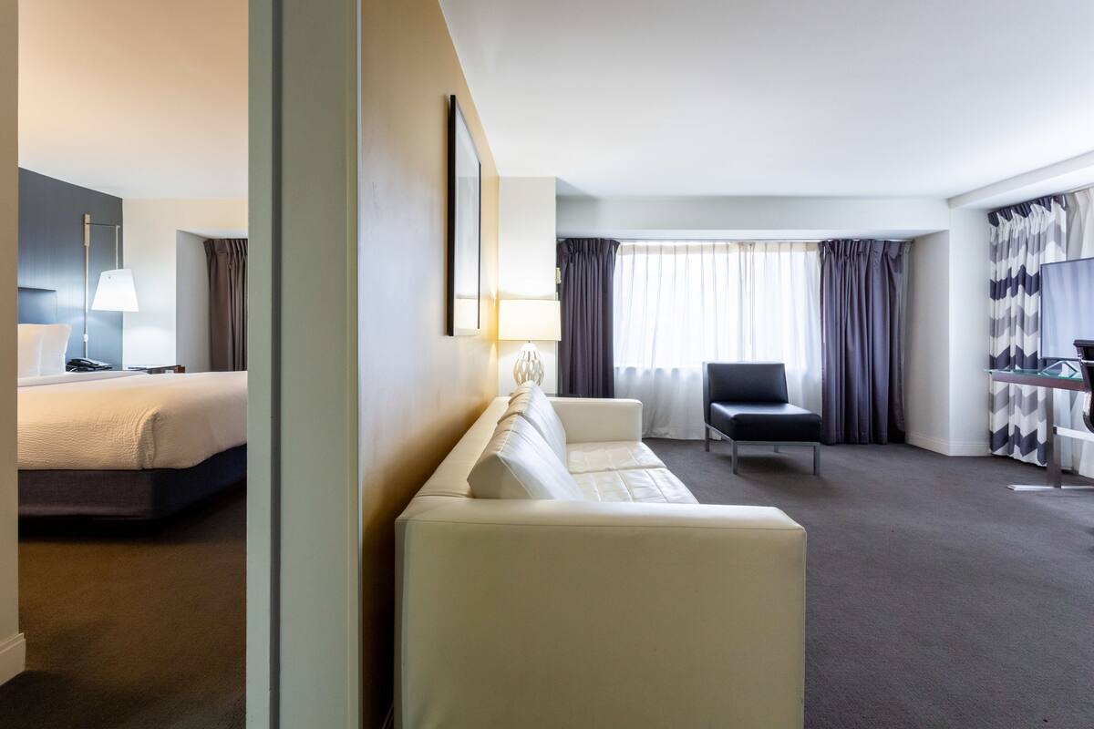 A hotel room with a bed, a sofa, a chair, a desk, and a large window with curtains.