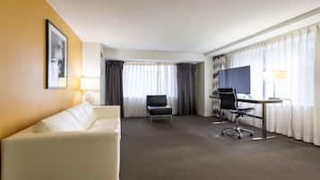 Habitación de hotel con un sofá blanco, un escritorio con computadora, una silla y un televisor.