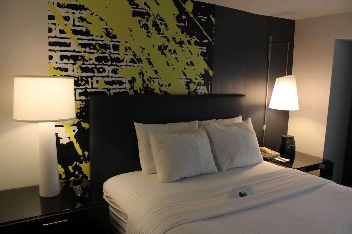 A hotel room with a large bed, two bedside tables, and a wall with a black and yellow abstract design.