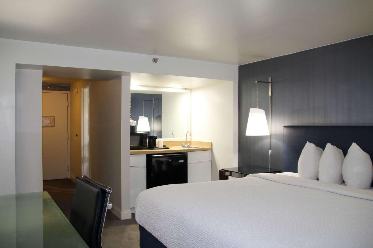 Ein Hotelzimmer mit Bett, Schreibtisch, Stuhl, Mikrowelle, Spüle und Spiegel.