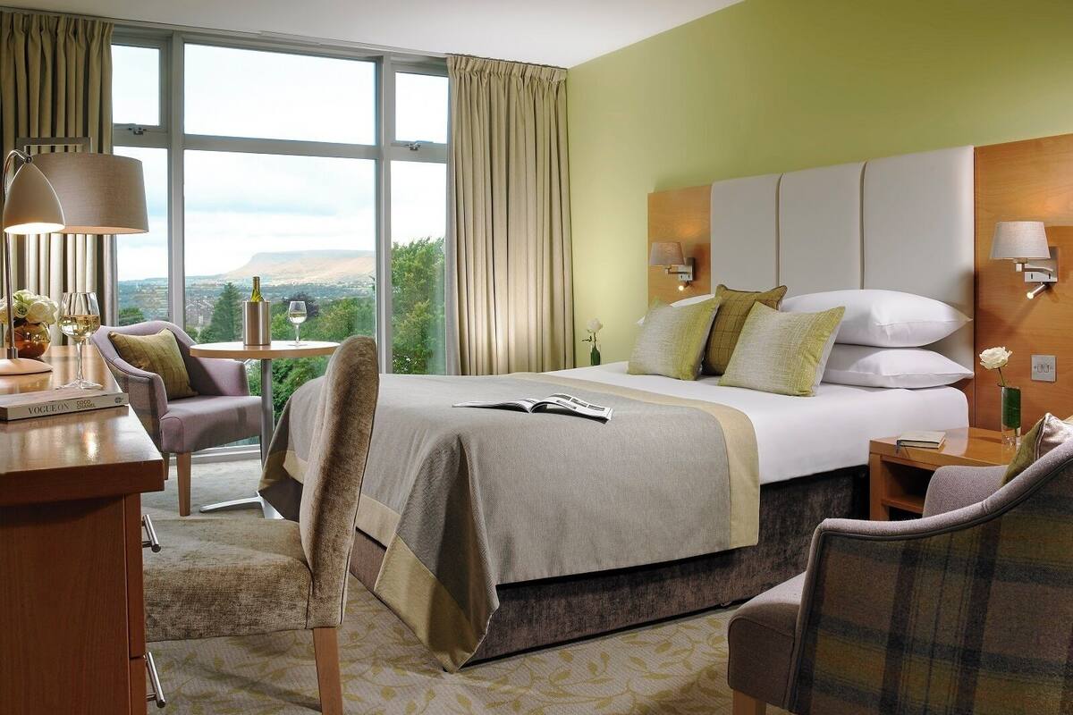 Une chambre d’hôtel avec un grand lit, un bureau avec une lampe, une chaise et une vue sur l’extérieur.