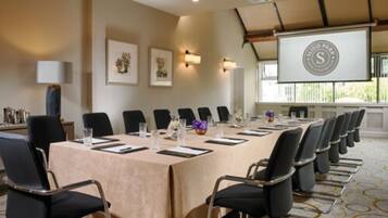 A conference room with a long table, black chairs, and a projector screen displaying a logo.