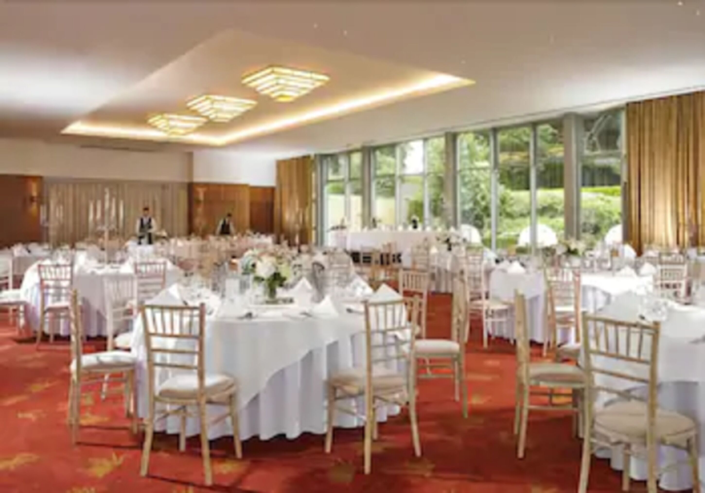 A banquet hall with round tables, white tablecloths, and wooden chairs.
