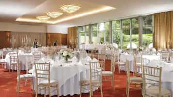 A banquet hall with round tables, white tablecloths, and wooden chairs.