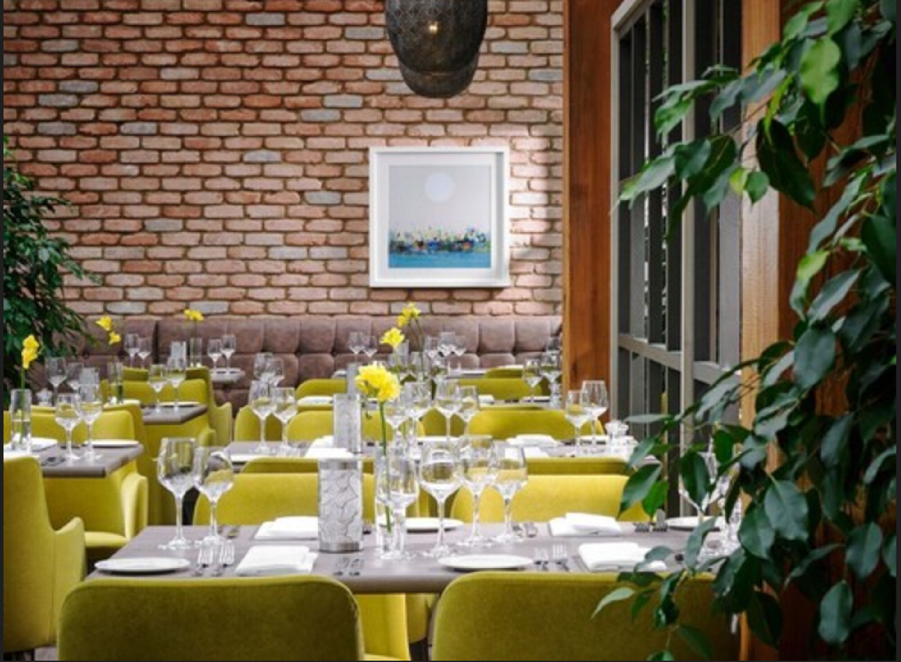 Un restaurante con sillas y mesas amarillas, una pared de ladrillo y un ventanal grande.