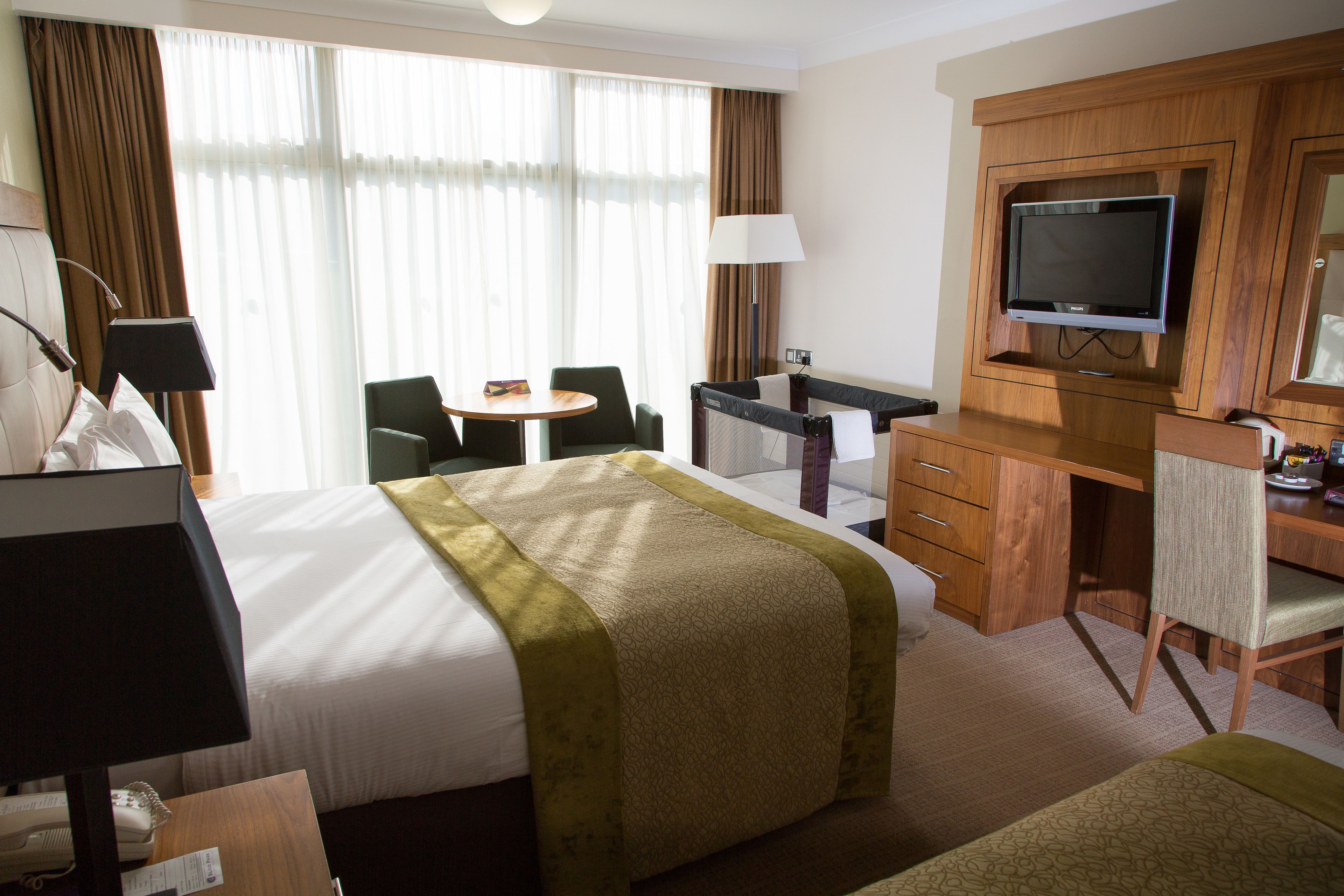 A hotel room with a bed, a desk, a chair, a television, and a window with curtains.