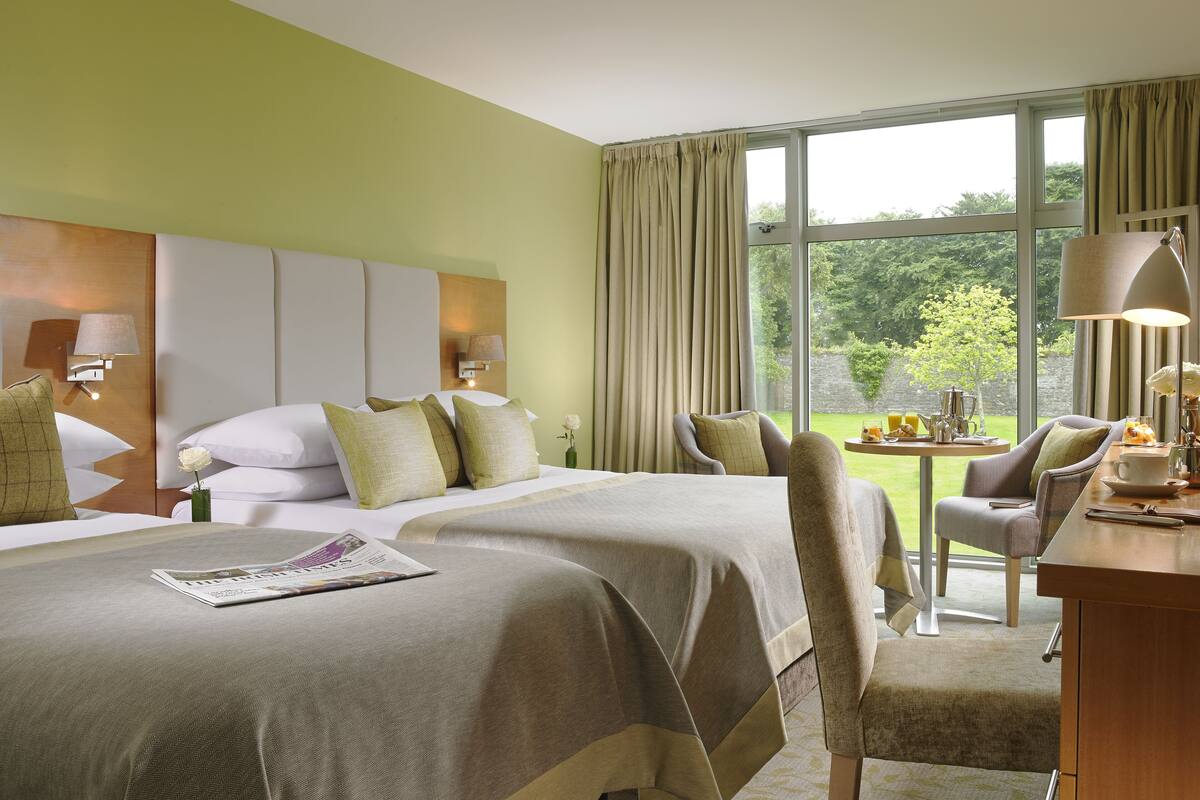 Une chambre d’hôtel avec un grand lit, un bureau avec une lampe et une vue sur le jardin.