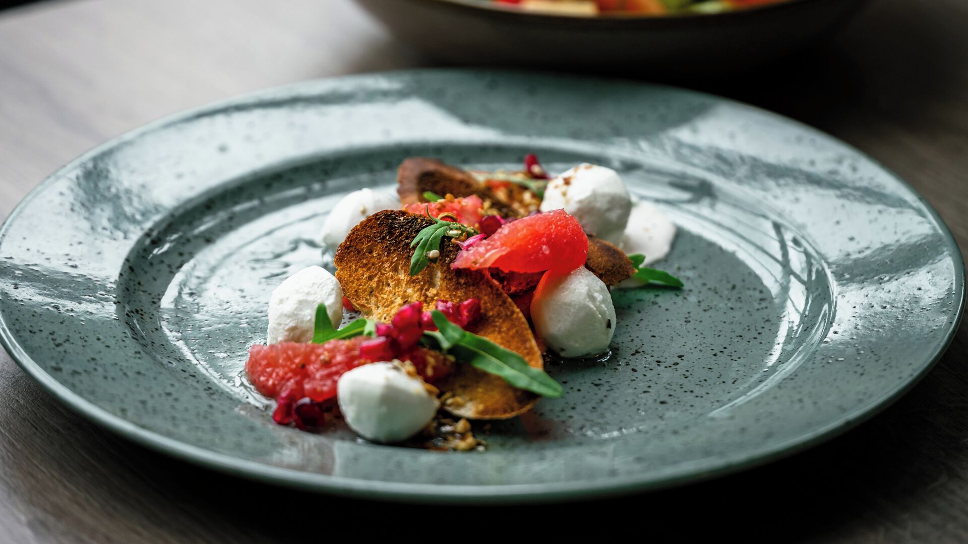 Un plato con un guiso de pan tostado, bolas de mozzarella y un aderezo rojo, posiblemente una fruta o verdura.
