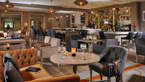 Zona de bar moderna con mesas redondas, taburetes y una amplia selección de licores.