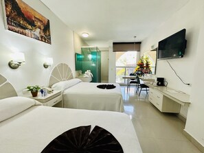 A hotel room with two beds, a desk, a TV, and a bathroom.