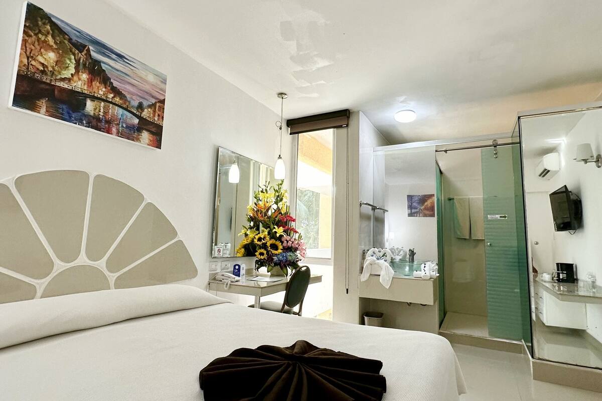 A hotel room with a bed, a desk, a chair, a bathroom, and a TV.