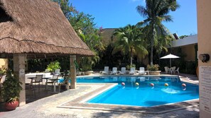 A pool area with lounge chairs, a thatched-roof structure, and a sign indicating pool regulations.
