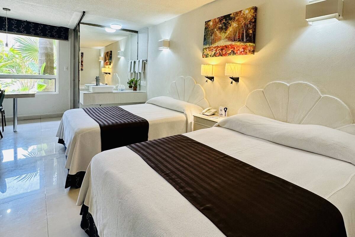 A hotel room with two beds, a bathroom, and a view of greenery outside.