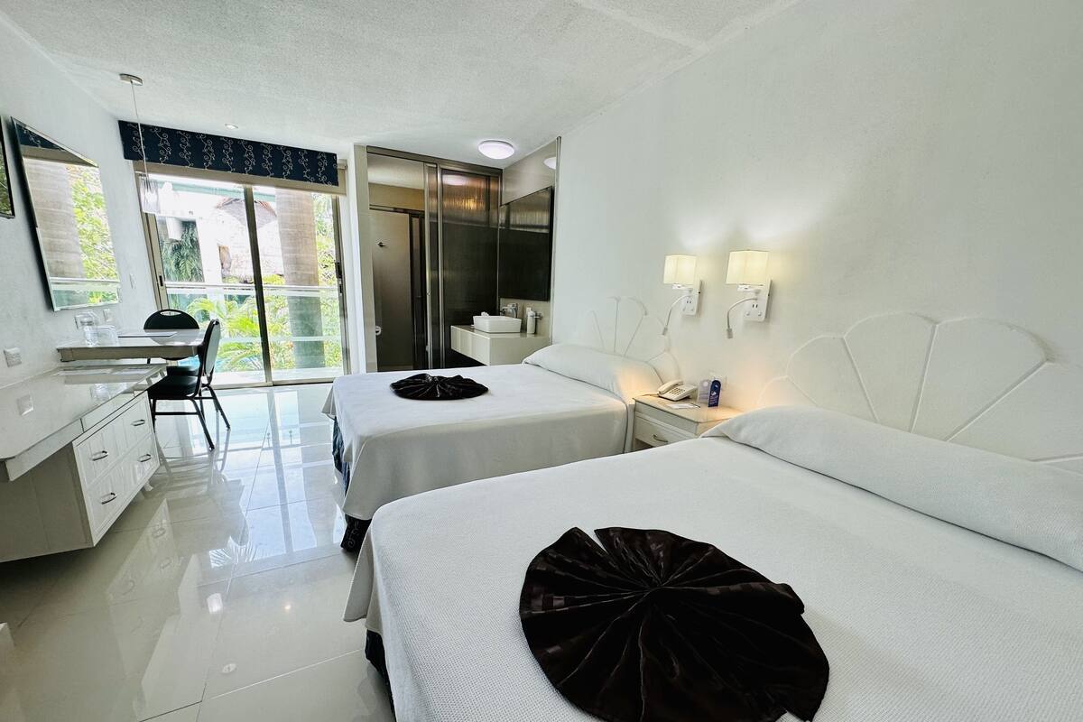 A hotel room with two beds, a desk, and a bathroom.