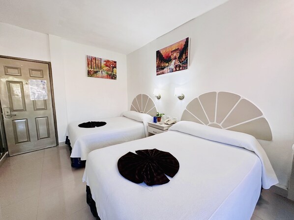 Habitación de hotel con dos camas, una puerta y dos cuadros colgados en la pared.